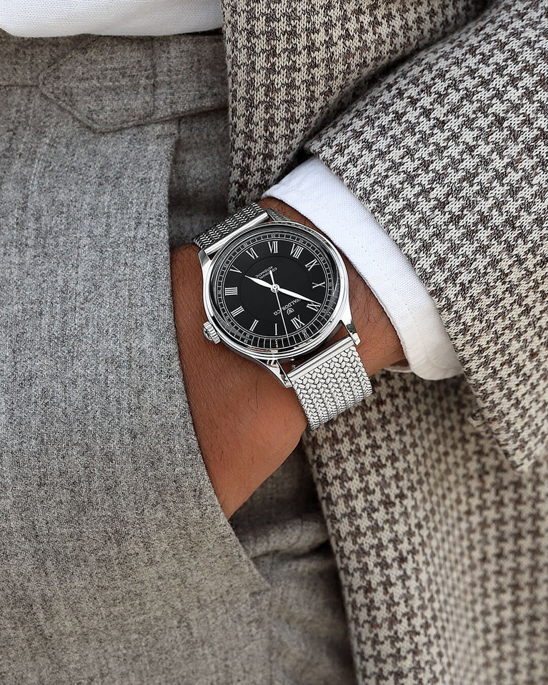 A round Automatic mens watch in Rhodiun plated 316L stainless from Waldor & Co. wit black double-layered dial in copper. Curved mineral glass with anti-reflective coating.Miyota 9093 movement. Mesh strap. The model is Continual 39 Amalfi.