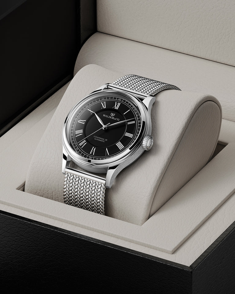 A round Automatic mens watch in Rhodiun plated 316L stainless from Waldor & Co. wit black double-layered dial in copper. Curved mineral glass with anti-reflective coating.Miyota 9093 movement. Mesh strap. The model is Continual 39 Amalfi.